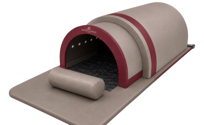 Un sauna infrarouge portable beige et bordeaux en forme de tunnel avec un tapis